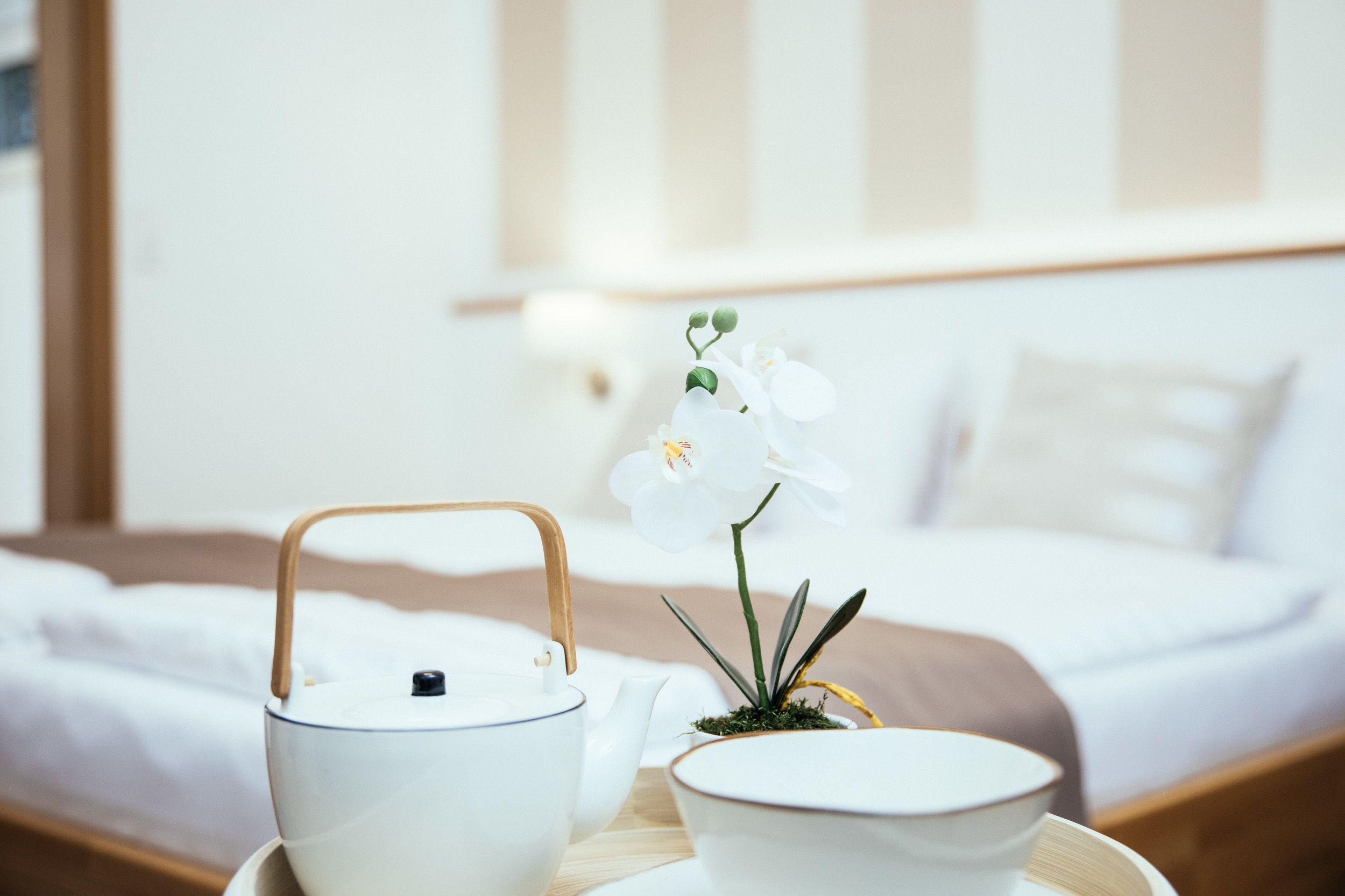 A neatly made bed with a white and brown striped headboard, a bedside table with a white teapot, a white cup, and a small potted plant.