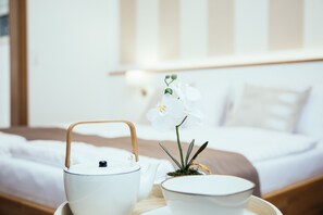 Un lit bien fait, avec une tête de lit rayée de blanc et de marron, une table de chevet sur laquelle se trouvent une théière blanche, une tasse blanche et une petite plante en pot.