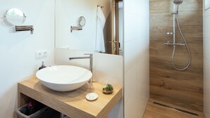 Ein modernes Badezimmer mit einem großen Spiegel, einem Holzbadezimmer-Möbelstück, einem weißen Waschbecken und einer Dusche mit einer Wandverkleidung aus Holz.