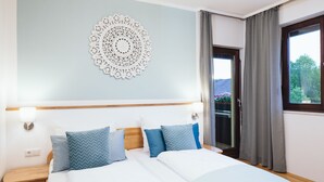 Ein ordentlich bezogenes Bett mit blau-weißer Bettwäsche, ein hölzernes Kopfteil, ein Wanddekor und ein Fenster mit Vorhängen.