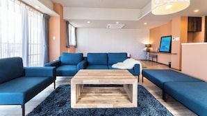 A modern living room with a blue sofa set, a wooden coffee table, and a black shag rug. - Breaky HOTEL (Chatan)