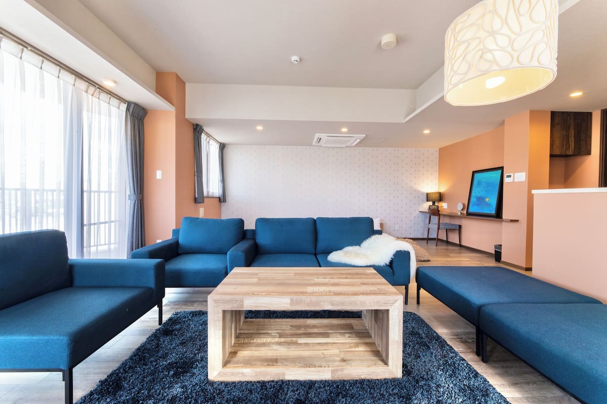 A modern living room with a blue sofa set, a wooden coffee table, and a black shag rug.