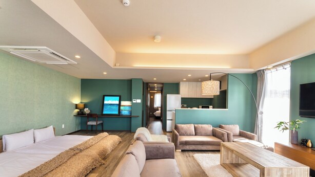 A modern hotel room with a large bed, two sofas, a wooden coffee table, and a TV. - Breaky HOTEL (Chatan)