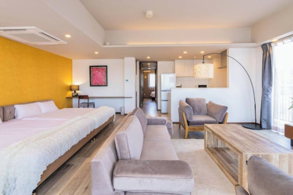 A modern hotel room with a large bed, a sofa, a desk, and a dining area.