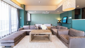 A modern living room with a sectional sofa, a wooden coffee table, and a large window with curtains. - Breaky HOTEL (Chatan)