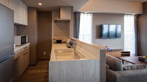 A modern kitchen with a built-in microwave, a sink, and a stove. There is a dining area with a sofa and a TV mounted on the wall. - Breaky HOTEL (Chatan)