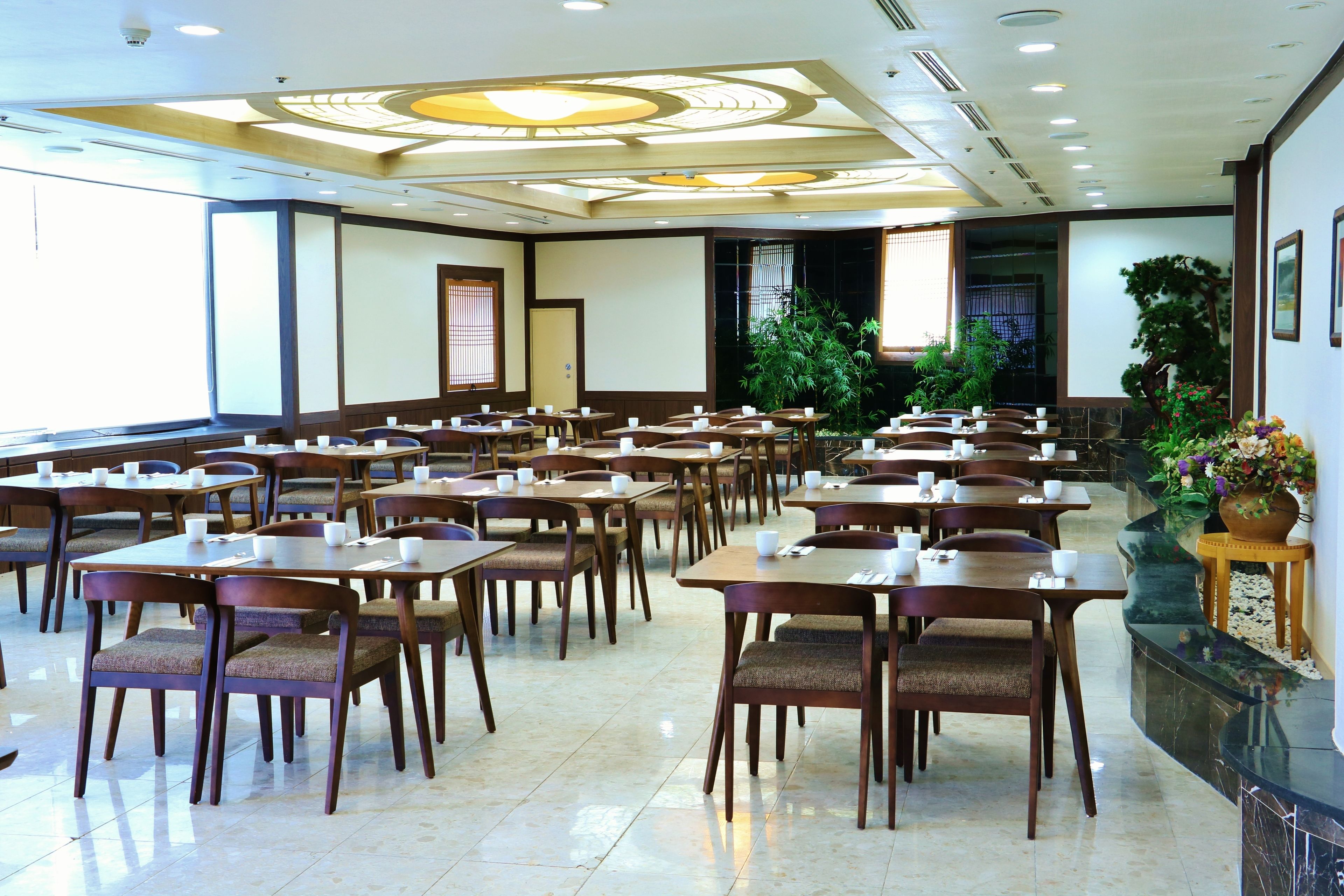 A hotel dining area with multiple tables and chairs, a large window, and a decorative ceiling.