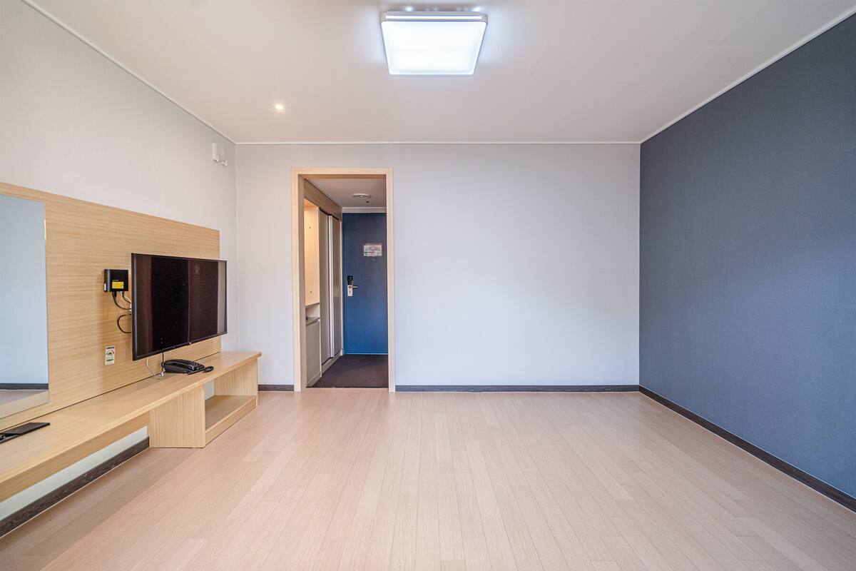 A modern hotel room with a wooden entertainment unit, a flat-screen TV, and a large mirror.