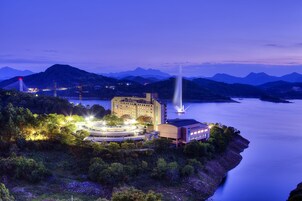 Un hotel costero con un edificio amplio, una fuente y montañas al fondo.