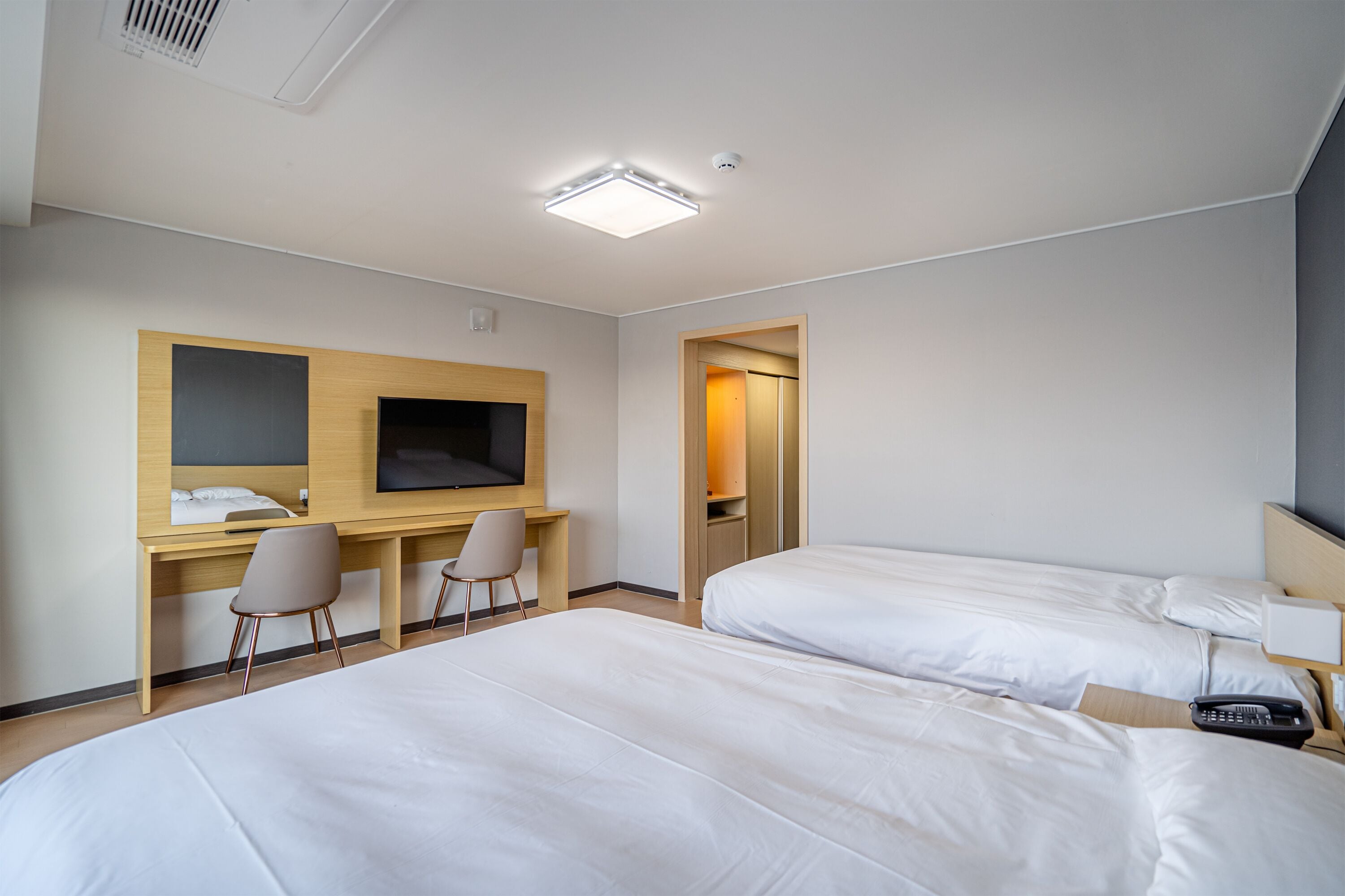 A hotel room with two beds, a desk with a chair, a television, and a door leading to a bathroom.