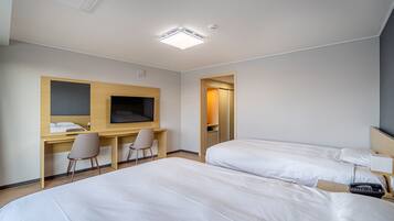 A hotel room with two beds, a desk with a chair, a television, and a door leading to a bathroom.