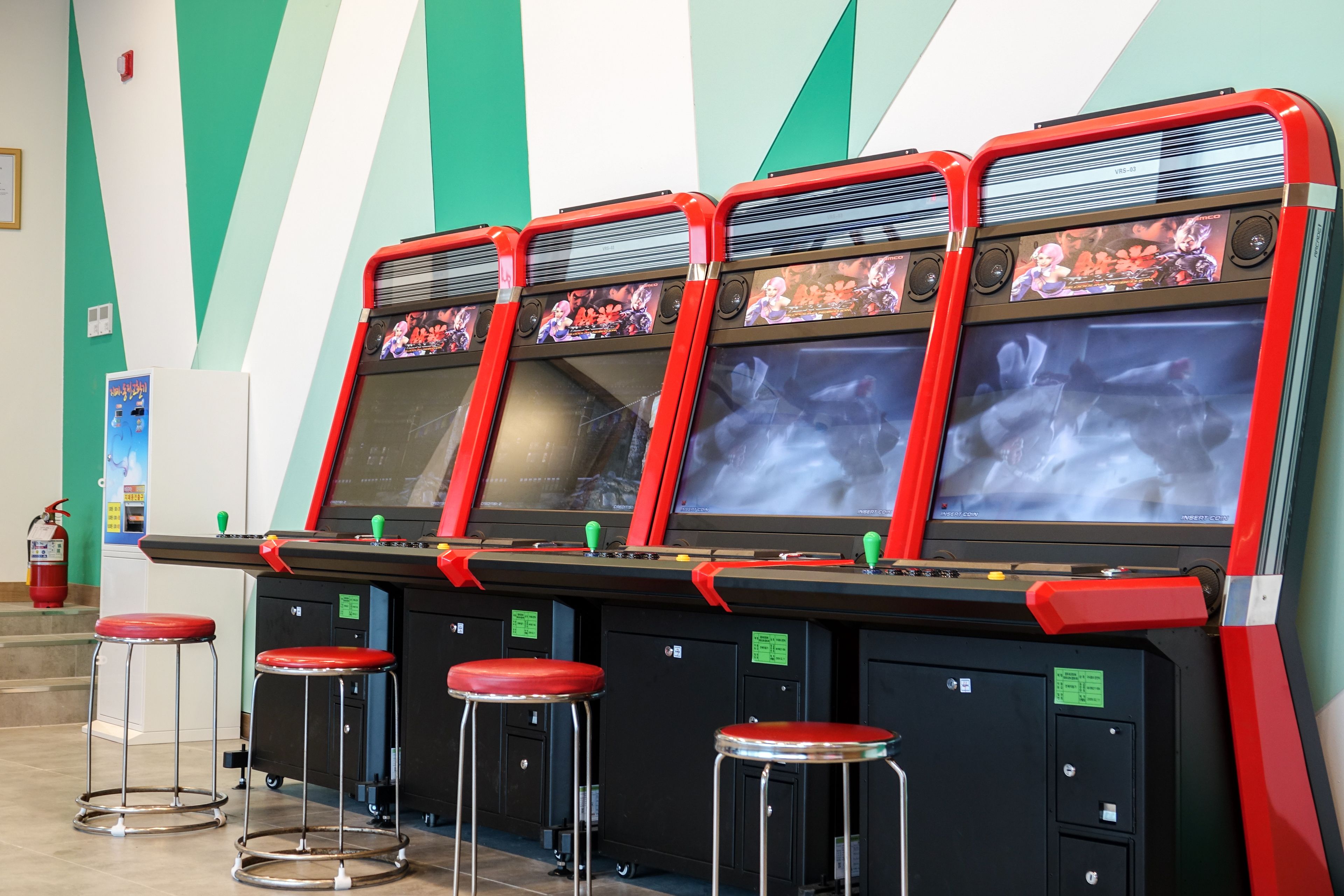 Cuatro máquinas de videojuegos de arcade con marcos rojos y mangos verdes, cada una con una pantalla mostrando gráficos de juego.