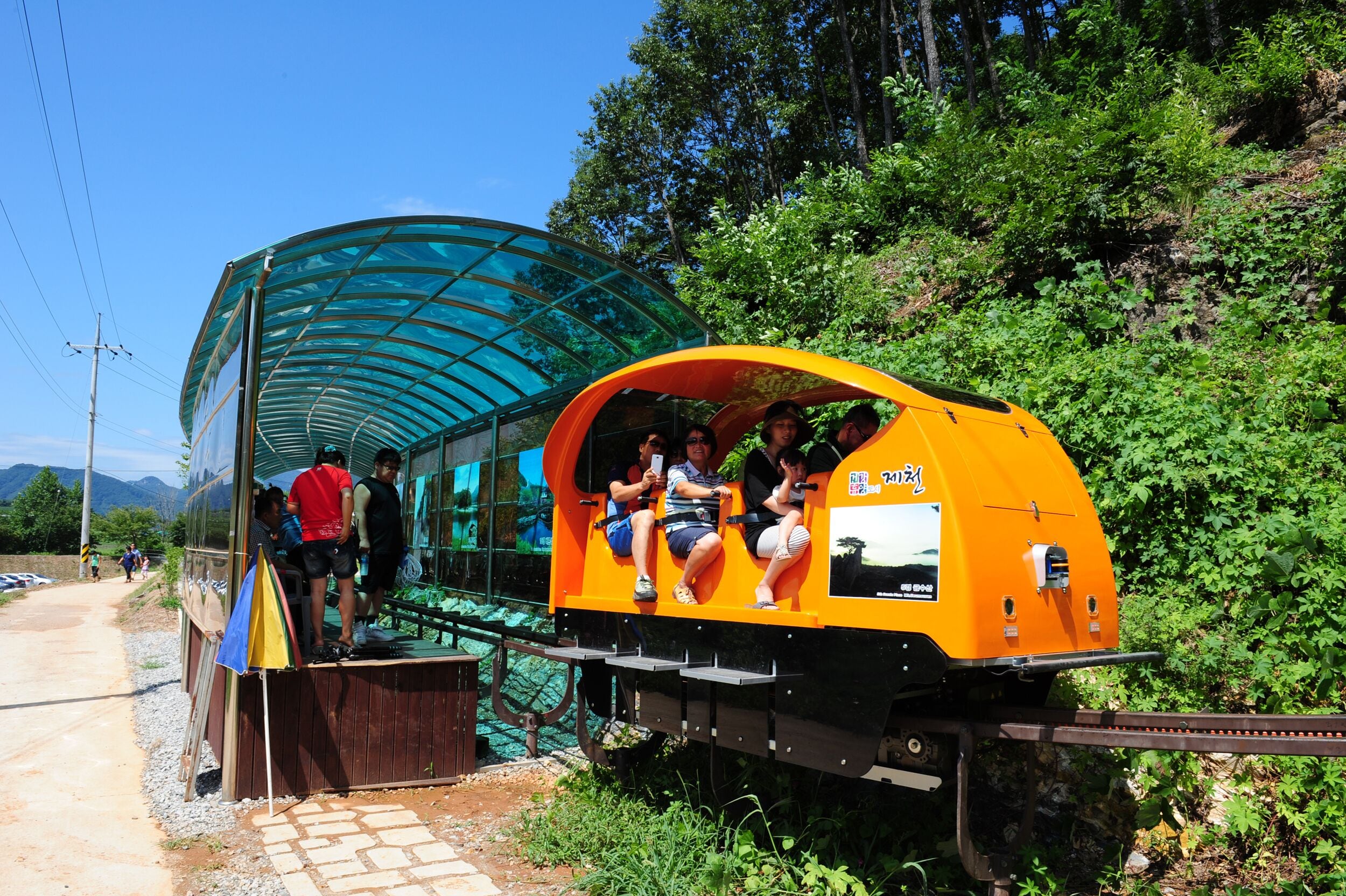 A small, enclosed train car with passengers seated inside, parked next to a covered walkway.