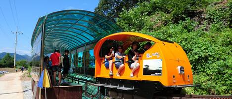 A small, enclosed train car with passengers seated inside, parked next to a covered walkway.