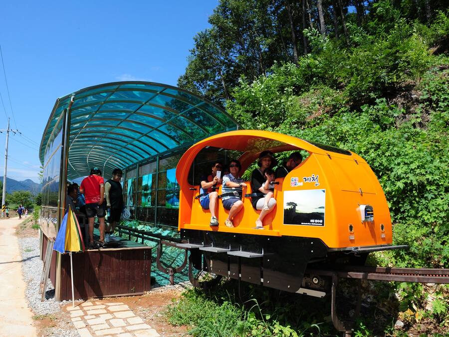 A small, enclosed train car with passengers seated inside, parked next to a covered walkway.