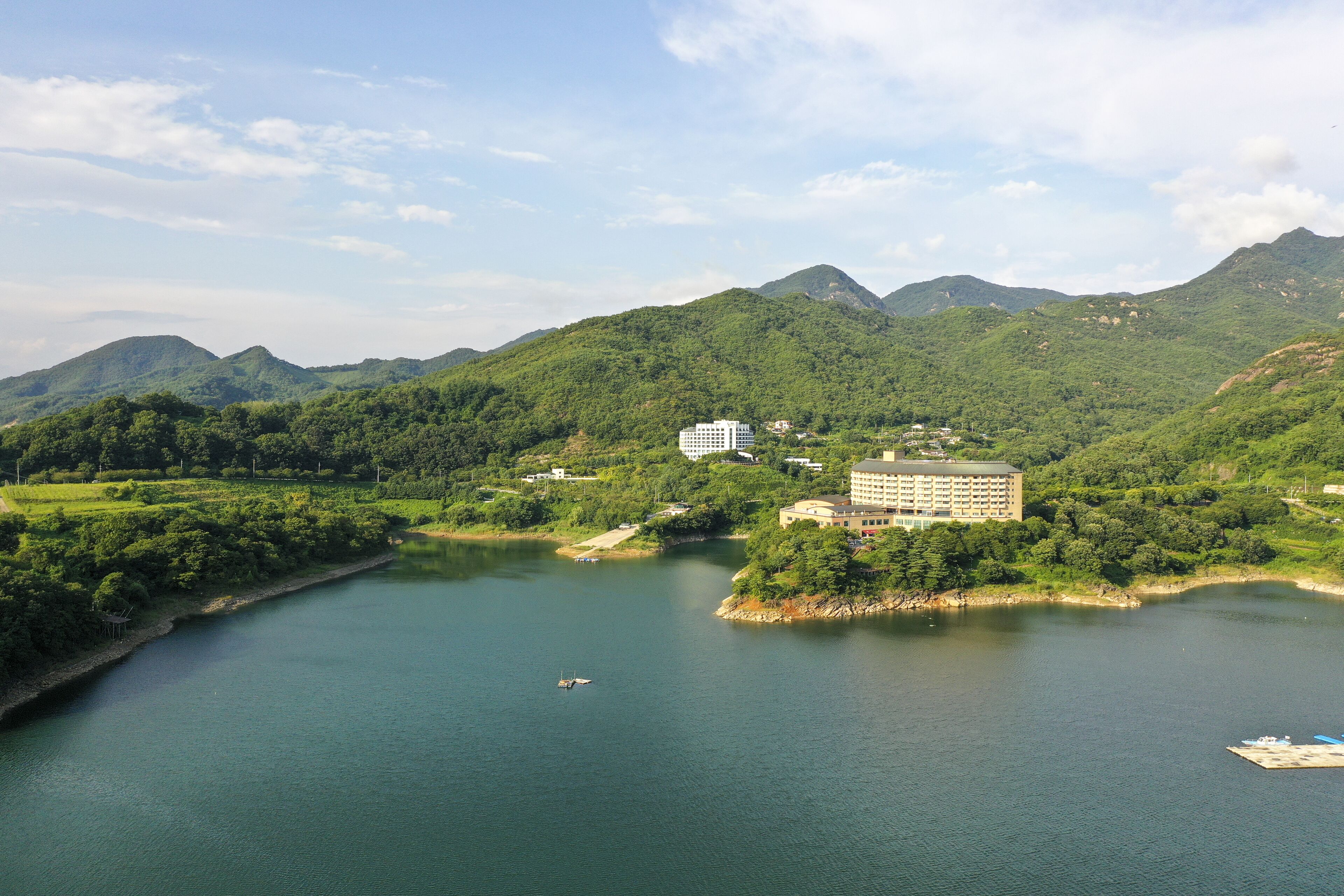 A hotel surrounded by lush greenery and mountains, with a body of water in the foreground.