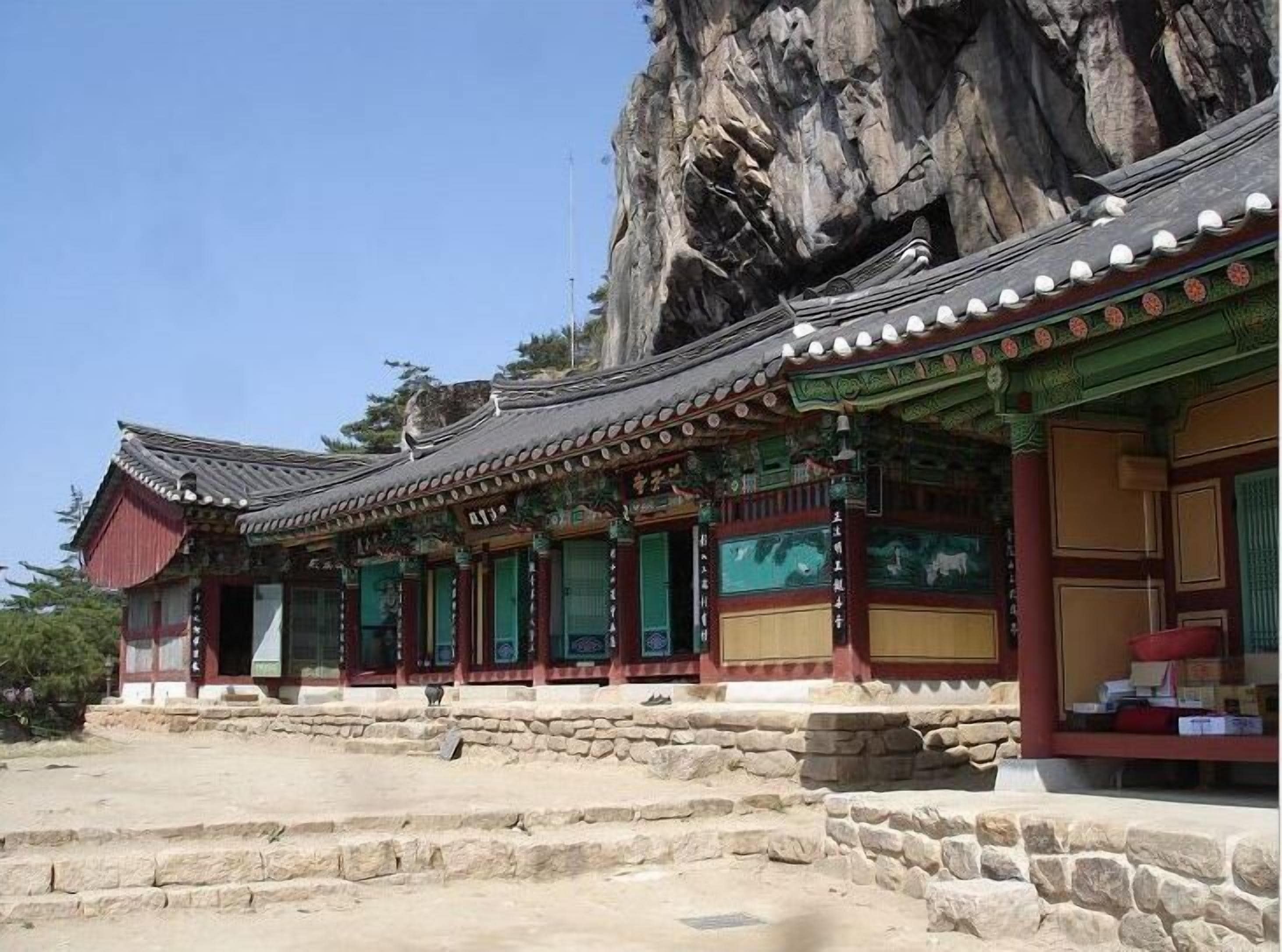 A traditional Korean building with a stone staircase leading to the entrance, set against a rocky cliff backdrop.