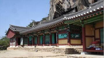 A traditional Korean building with a stone staircase leading to the entrance, set against a rocky cliff backdrop.