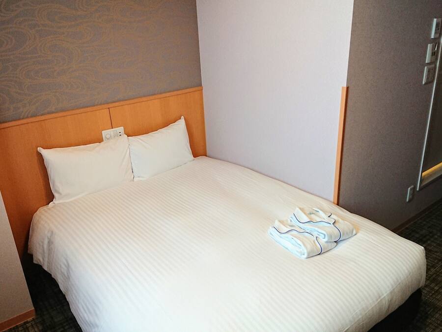 Una camera d'albergo con un letto, una testiera, un comodino e una parete con motivo decorativo.
