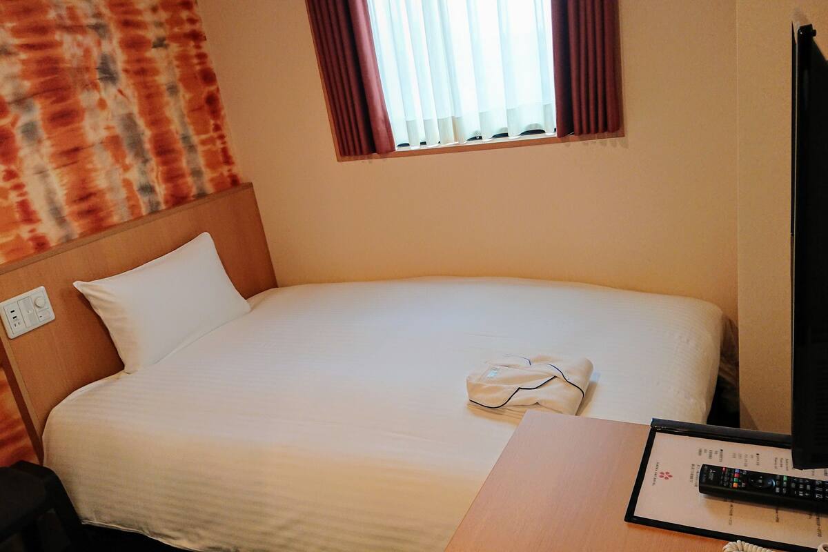 Une chambre d’hôtel avec un lit, une table de chevet avec une télécommande et une fenêtre avec des rideaux.