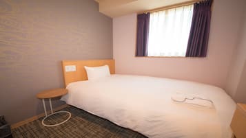 Habitación de hotel con una cama individual, una mesita redonda pequeña, un cesto de basura y una ventana con cortinas.