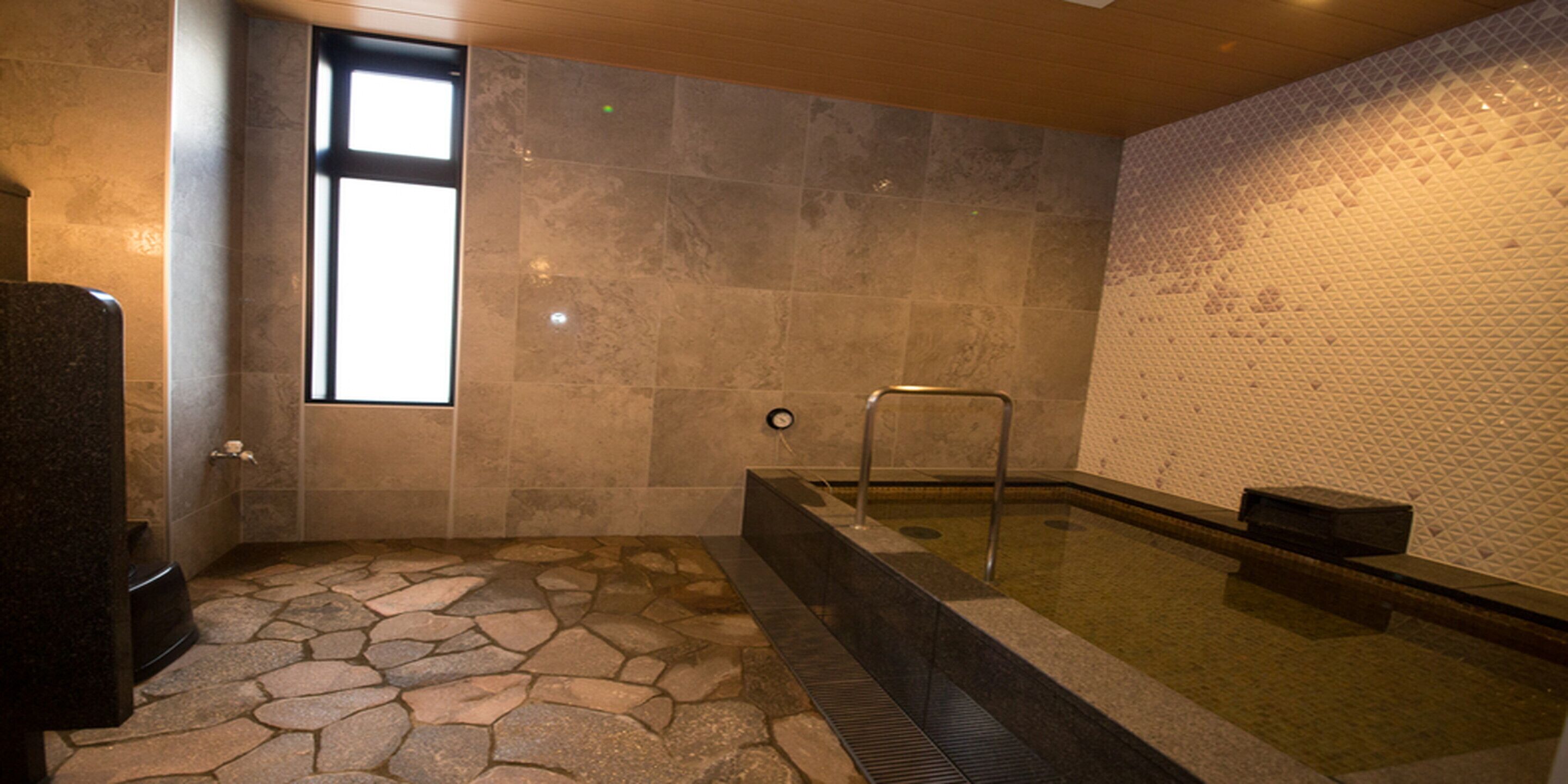 Un espace spa doté d’un sol en pierre, d’un bain à remous et d’une fenêtre laissant entrer la lumière naturelle.