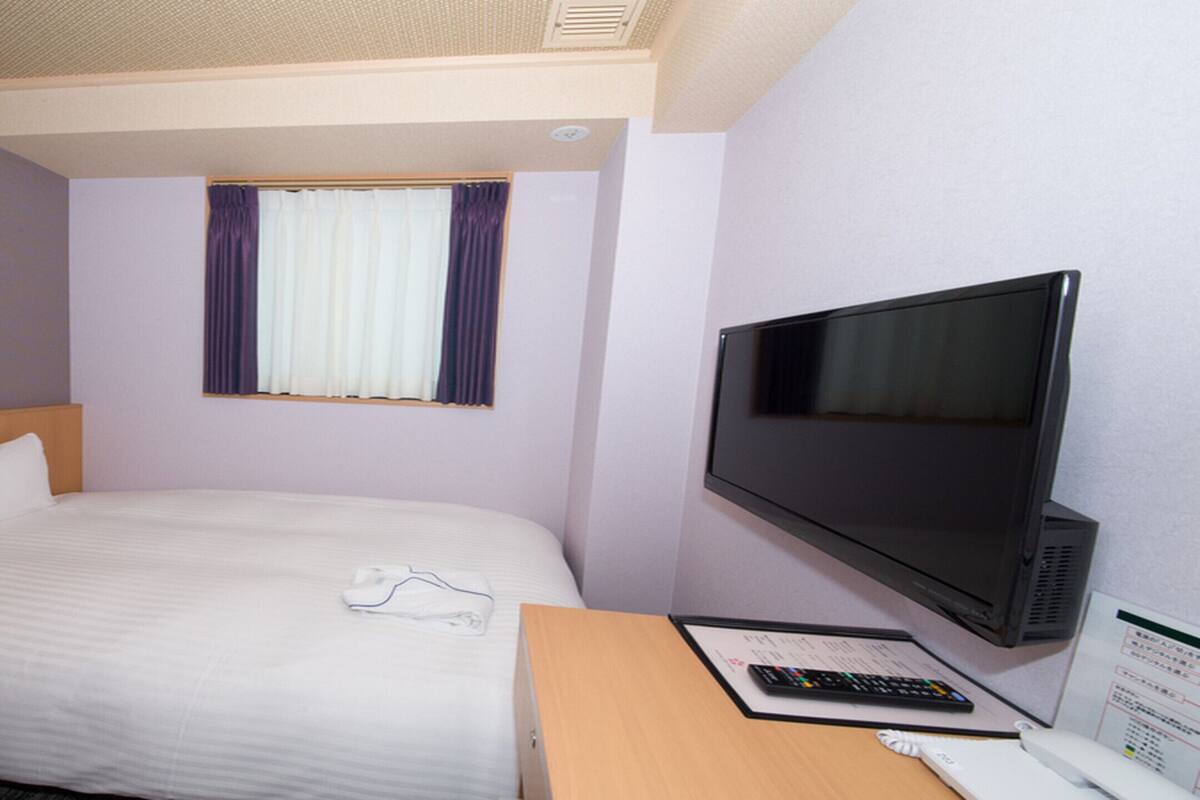 Une chambre d’hôtel équipée d’un lit, d’une télévision, d’un bureau avec une télécommande et d’une fenêtre avec des rideaux.