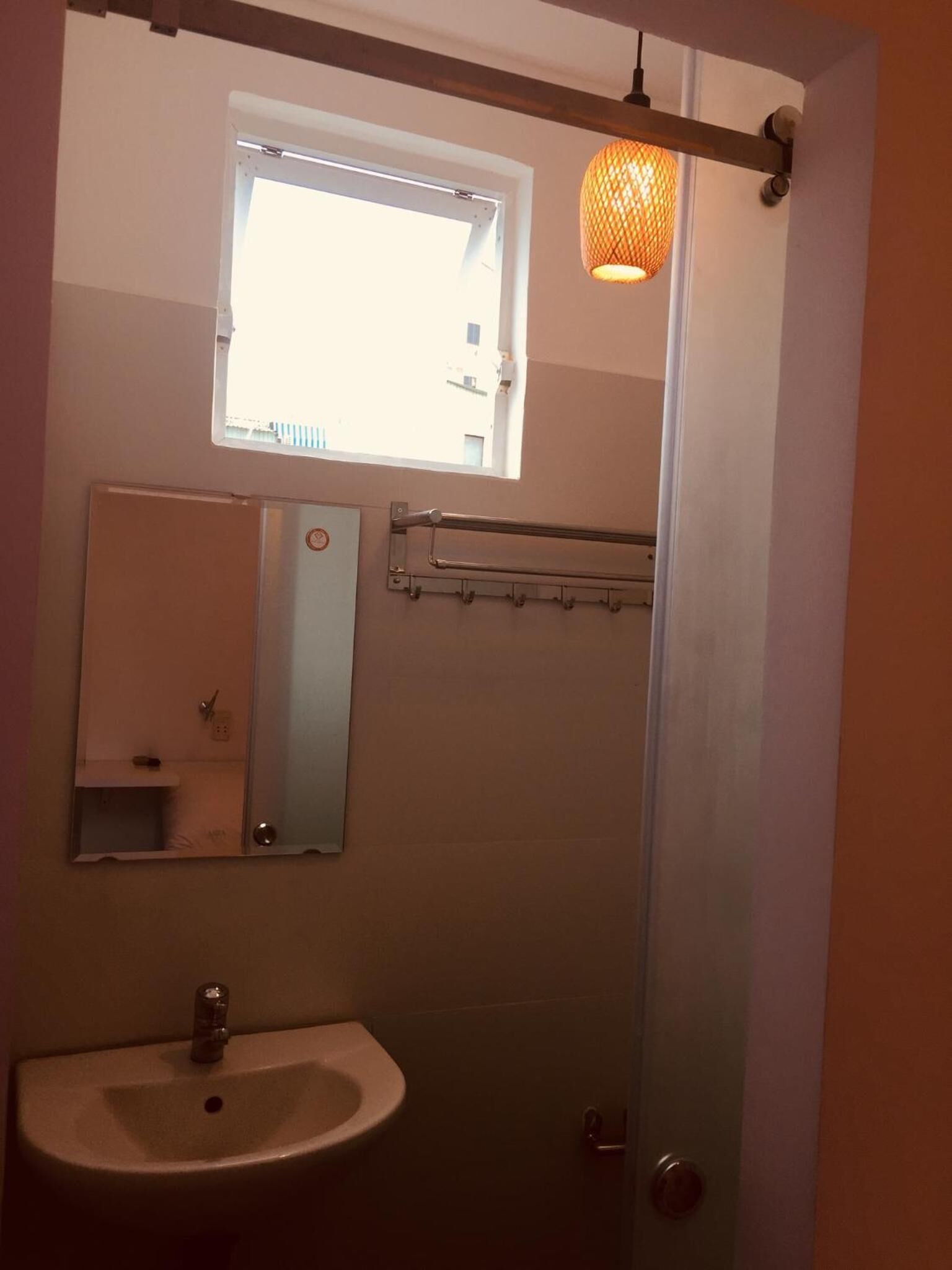 A bathroom with a window, a mirror, a sink, and a towel rack.