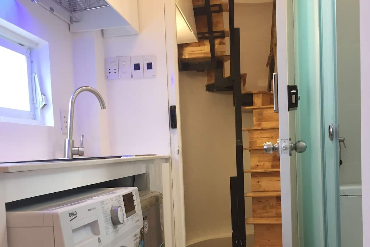 A compact kitchen with a washing machine, a sink, and a staircase leading to a wooden loft.