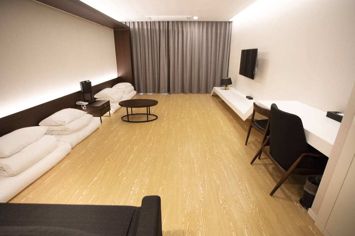 A hotel room with a bed, a sofa, a desk, a chair, a TV, and a curtain.