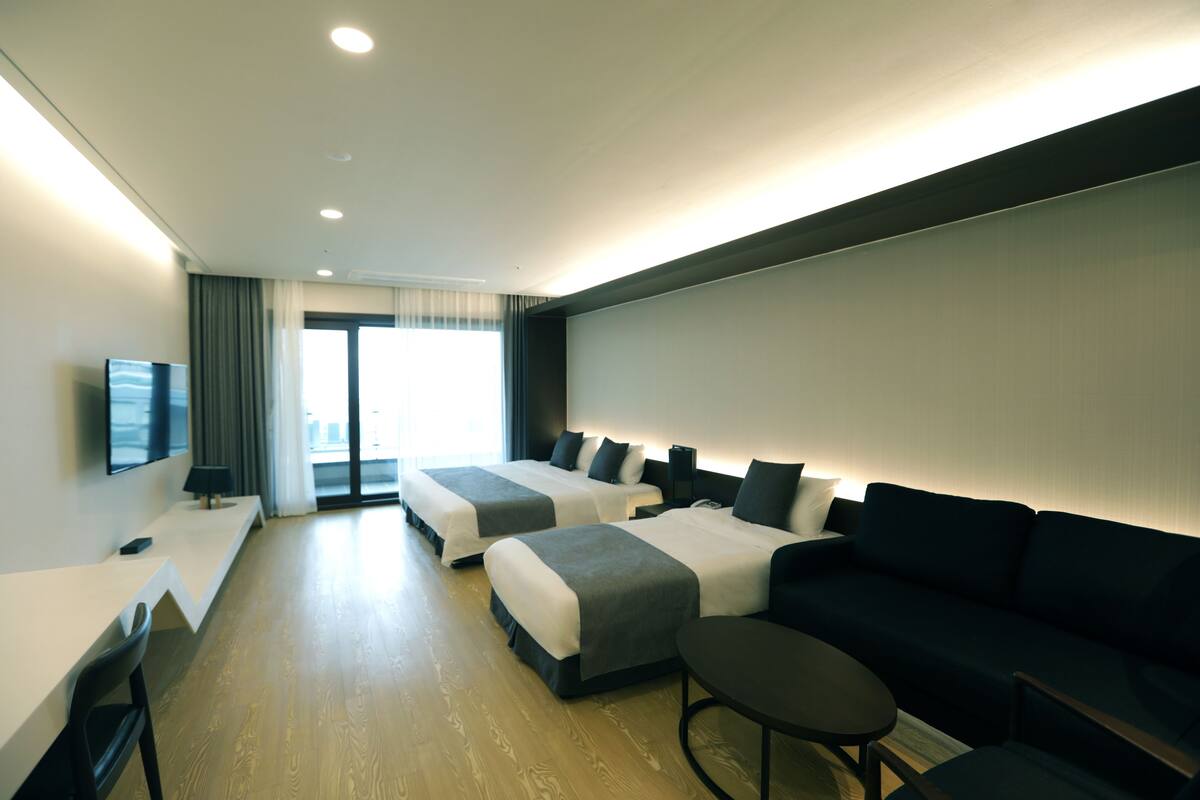 A hotel room with two beds, a sofa, a small table, and a TV.