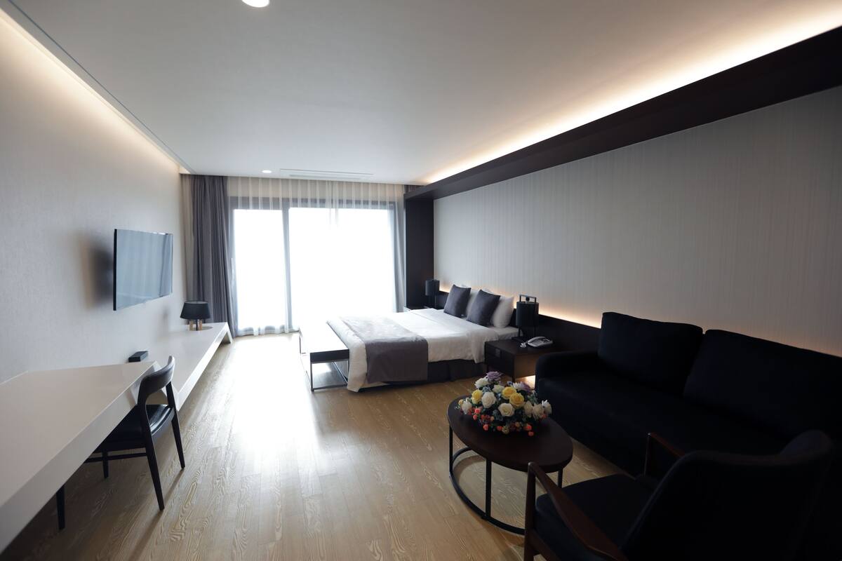 A modern hotel room with a bed, a sofa, a desk, and a TV.