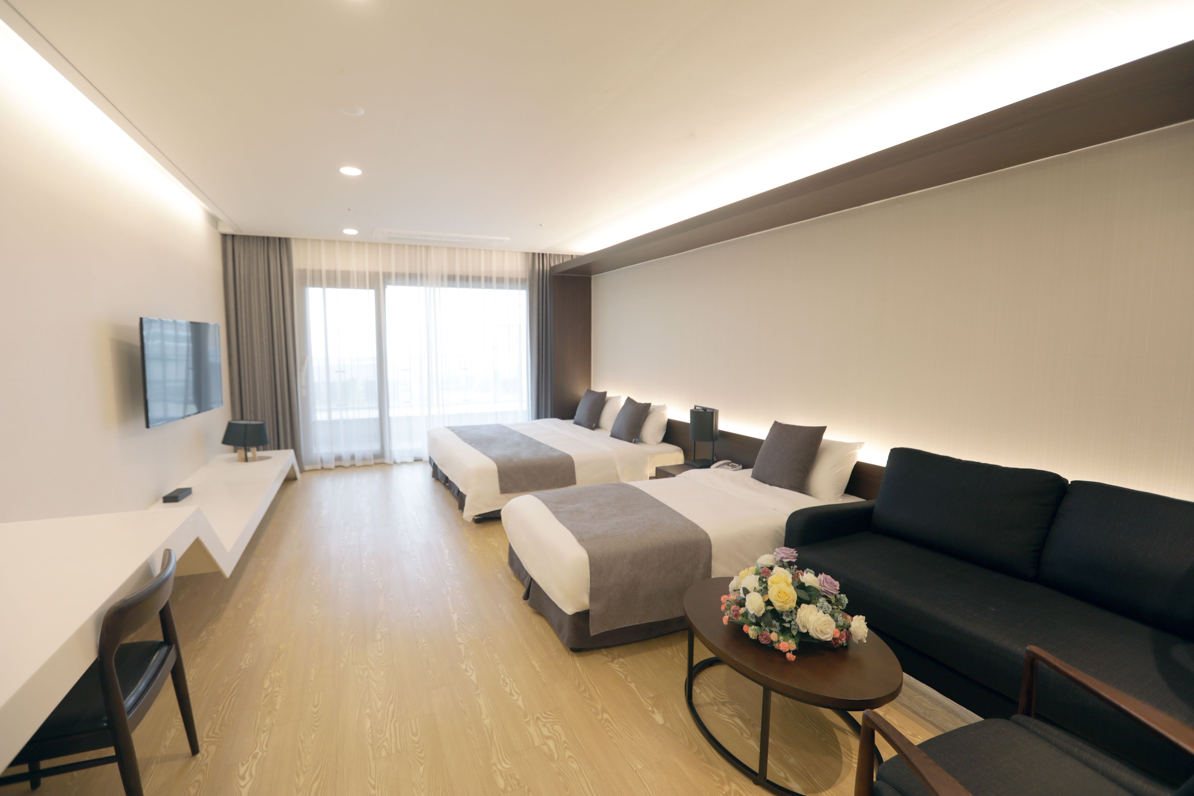 A hotel room with two beds, a sofa, a desk, and a TV.