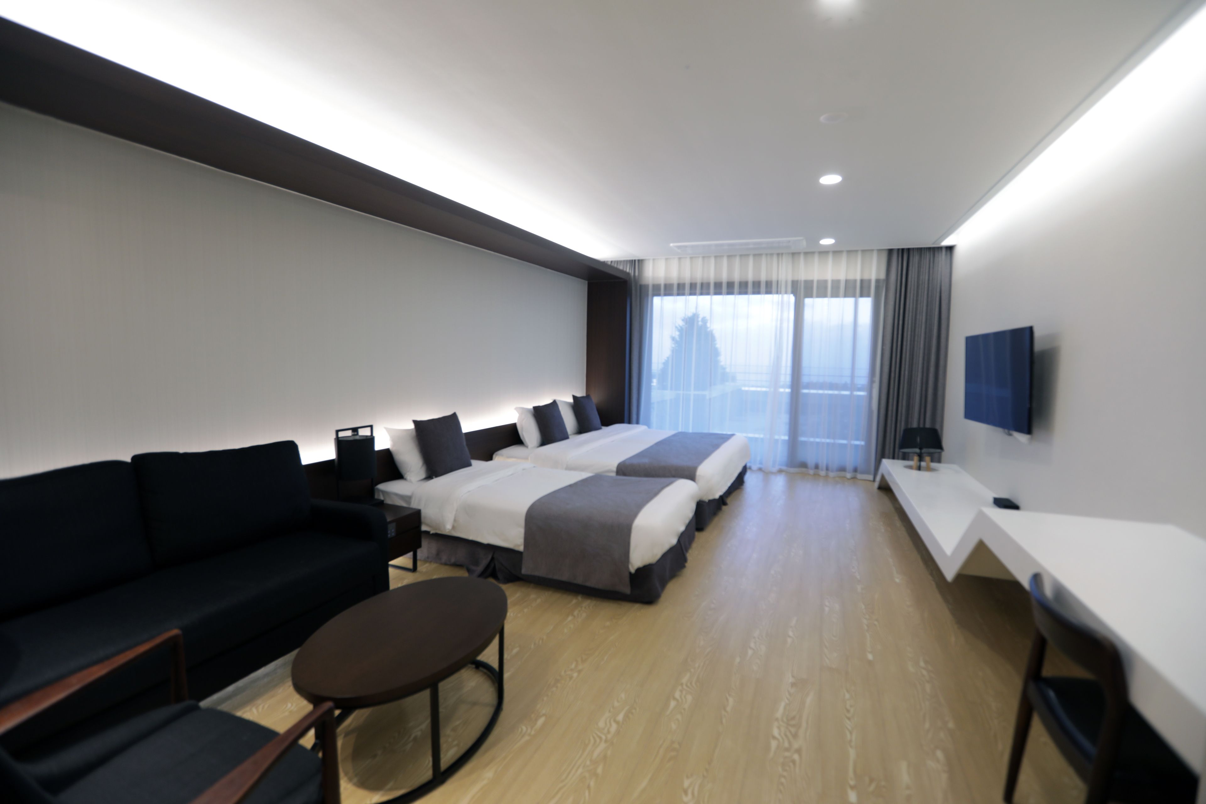 A modern hotel room with a sofa, two beds, a desk, and a TV.