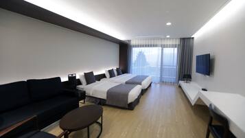 A modern hotel room with a sofa, two beds, a desk, and a TV.