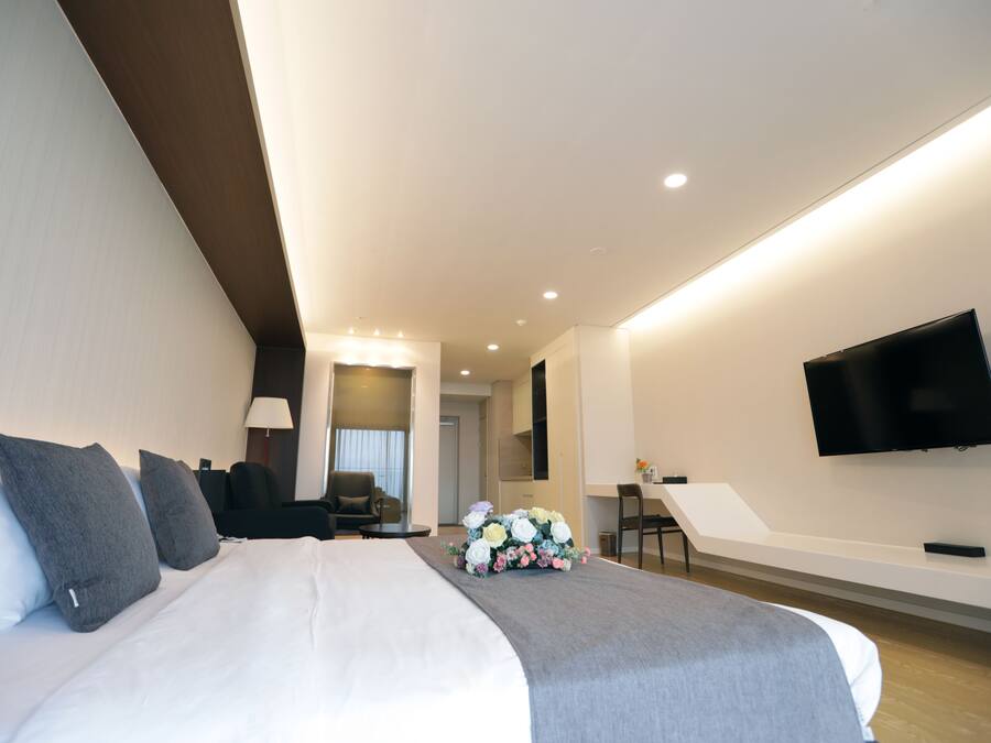 A modern hotel room with a large bed, a flat-screen TV mounted on the wall, and a desk with a chair.