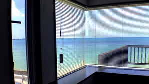 A room with a view of the sea through large windows with blinds, a balcony with a railing, and a door leading outside. - Pontoon (Ishigaki)