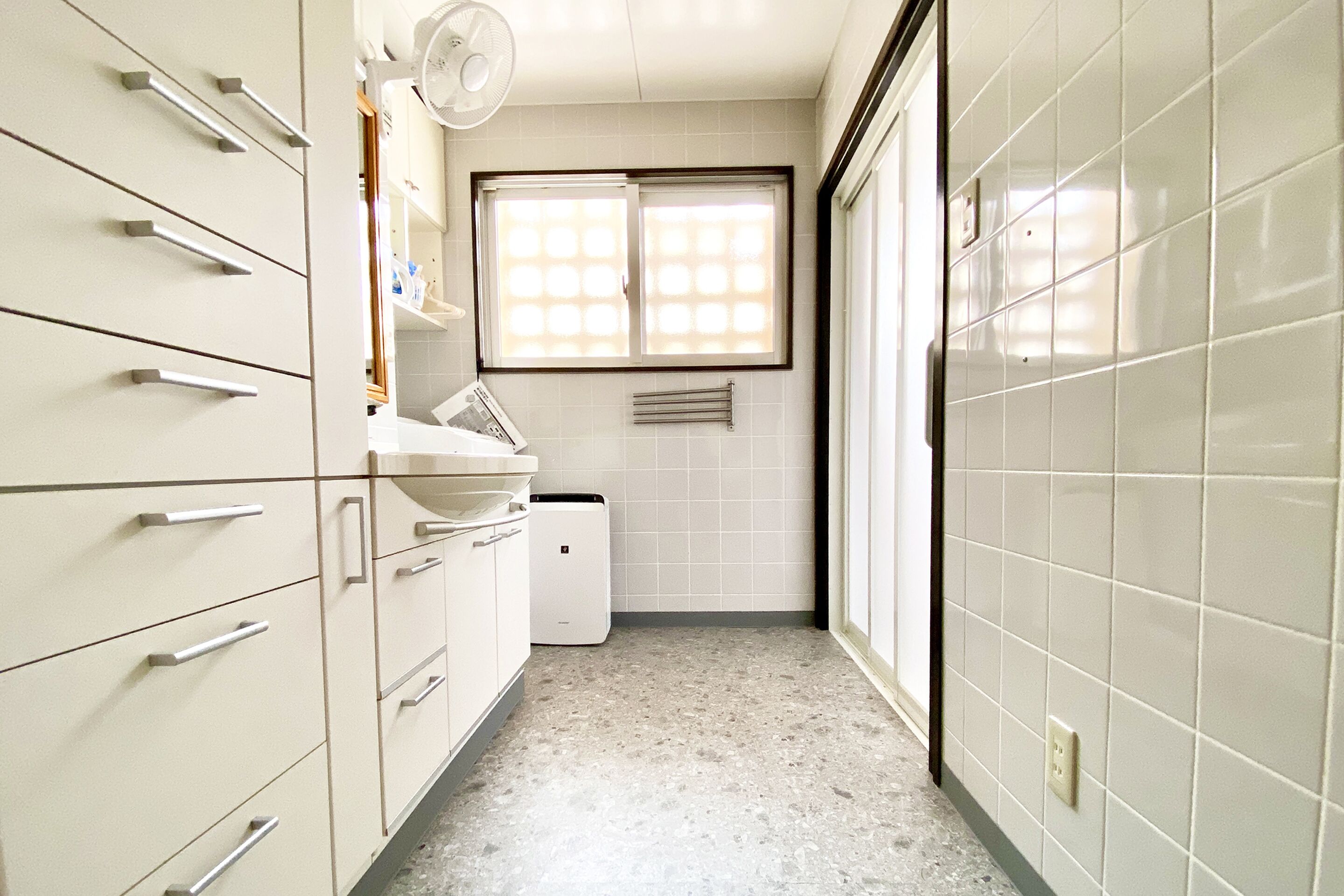 A narrow kitchen with white cabinets, a built-in sink, and a window with blinds.