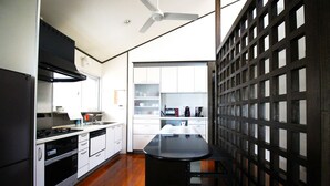 A compact kitchen with a black countertop, white cabinets, and a wooden stool. - Pontoon (Ishigaki)