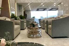 A modern lounge area with sofas and a coffee table, large windows, and a view of the outdoors. - Emerald Bay Hotel & Spa Nha Trang (Nha Trang)