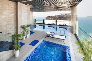 En pool på taket med utsikt över havet, omgiven av planterade växter och solstolar.