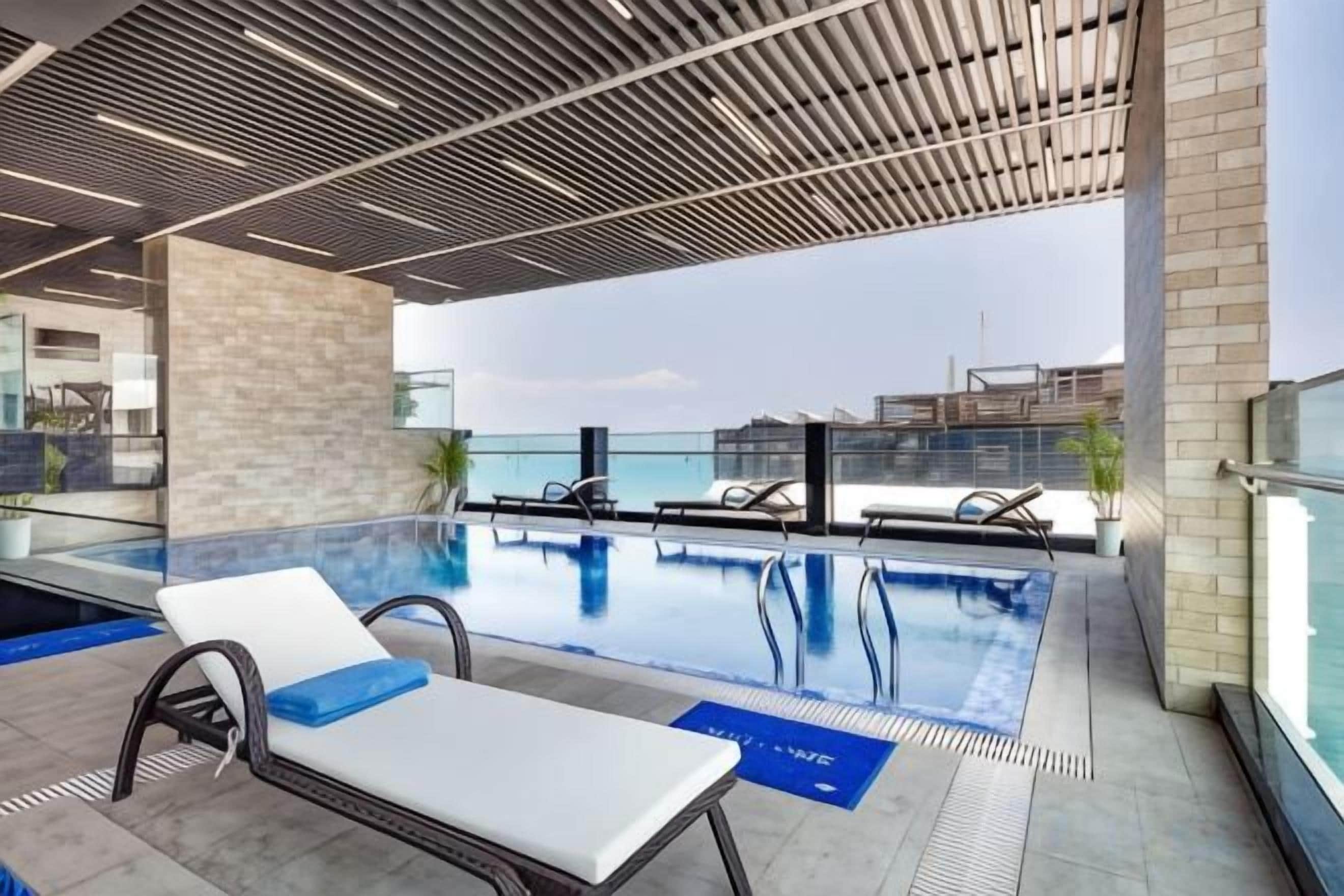 A rooftop swimming pool with lounge chairs and a view of the city skyline.