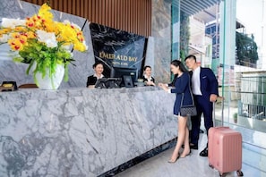 A hotel reception desk with a marble counter, a large floral arrangement, and a digital display. - Emerald Bay Hotel & Spa Nha Trang (Nha Trang)