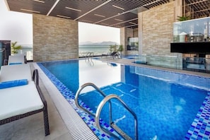 An indoor swimming pool with clear blue water, a poolside lounge area, and a view of the mountains in the background. - Emerald Bay Hotel & Spa Nha Trang (Nha Trang)