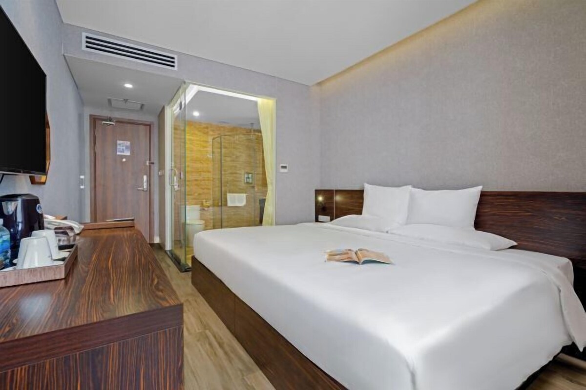 A hotel room with a bed, a desk with a coffee maker, a TV, and a shower area.