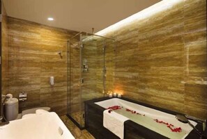 A modern bathroom with a glass-enclosed shower, a large bathtub with rose petals, and a wooden wall. - Emerald Bay Hotel & Spa Nha Trang (Nha Trang)
