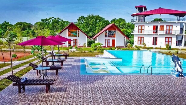 A swimming pool with lounge chairs and umbrellas, surrounded by buildings with red roofs and white walls. - Santon Resort & Spa (Kahandamodara)