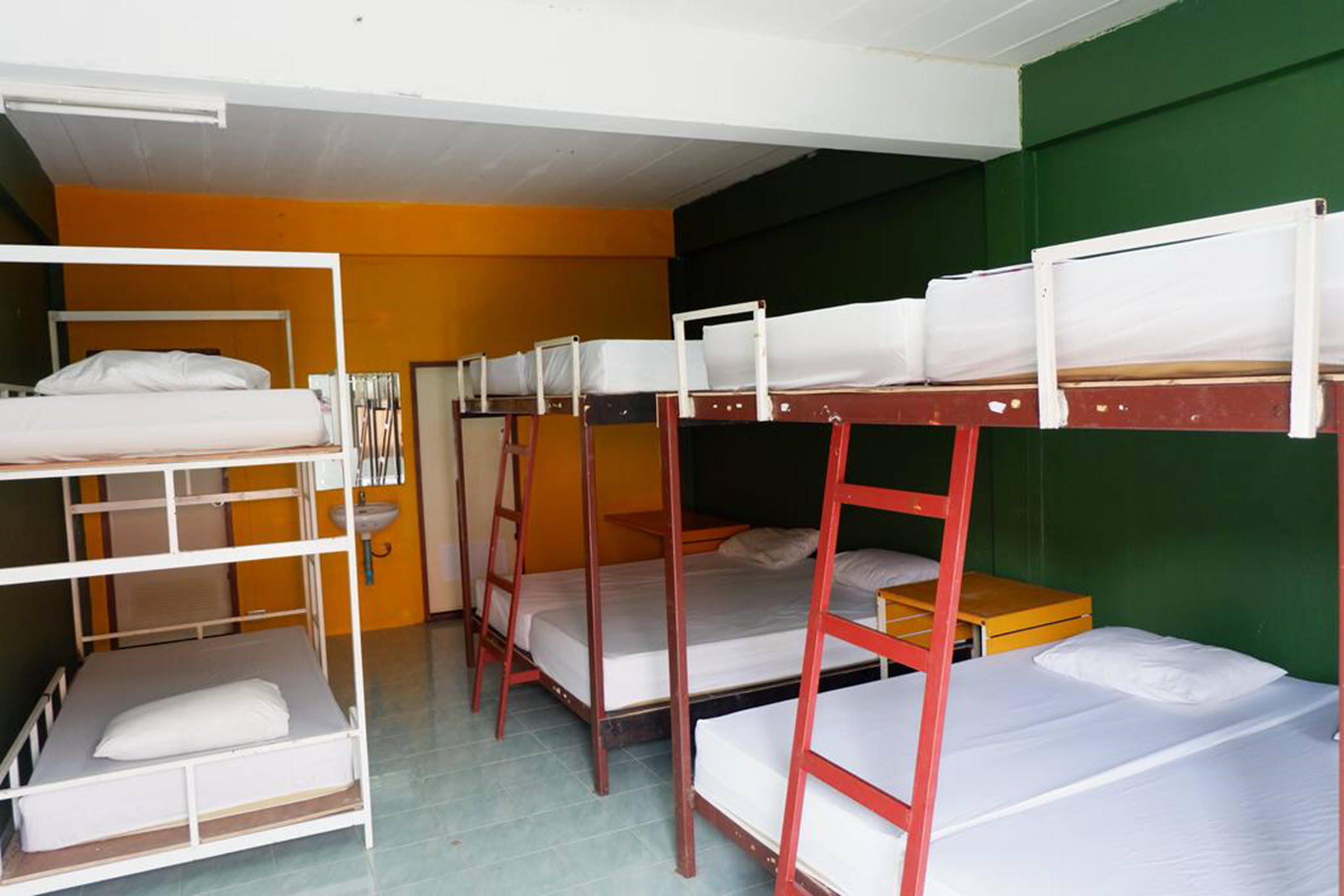 A dormitory room with bunk beds, a sink, and a mirror.