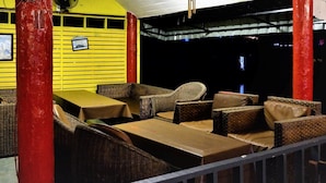 A restaurant with wicker furniture and tables, red pillars, and a yellow wall. - Jaya Hostel - Adults Only (Ko Pha-ngan)