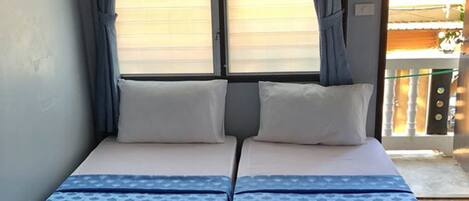 A room with two beds, a window with curtains, and a view of the outside.